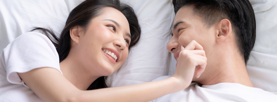 ベッドの上で、男性の頬をつねる女性