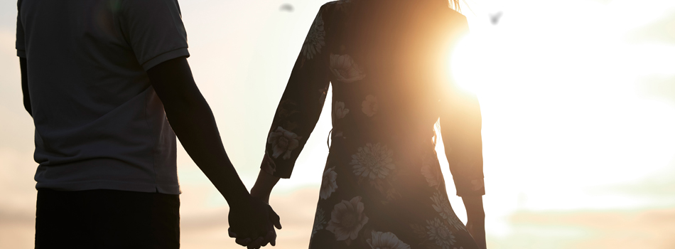 夕焼けを見ながら手を繋ぐカップル