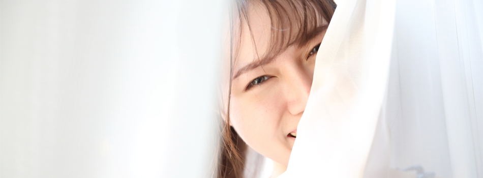 カーテンの隙間から顔を覗かせる笑顔の女性