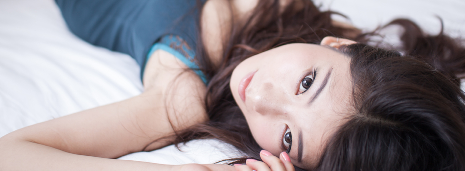 ベッドの上で仰向けになりながらこちらを見ている女性