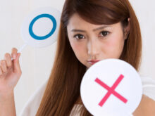 ×マークの札を向けてくる女性